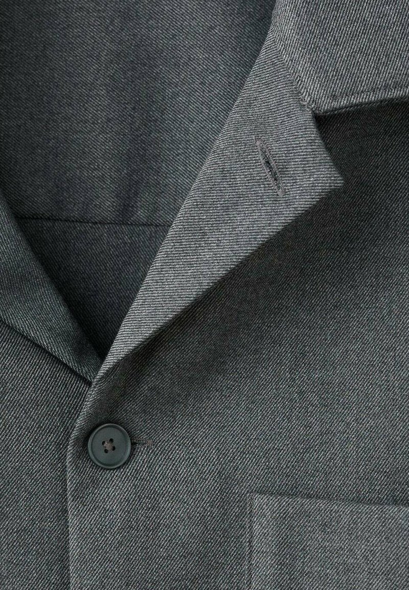 Grijze geweven stoffen blazer met een notch-kraag, een enkele knoopsluiting en een borstzak met subtiele stikseldetails.