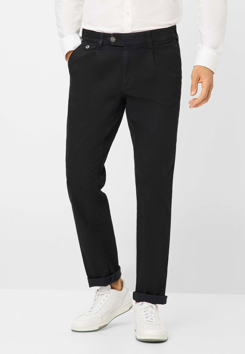 Chinos neri aderenti con una texture liscia, dotati di chiusura a bottone, tasche e orli arrotolati, abbinati a sneakers bianche.