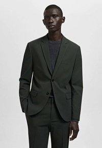 Dunkelgrüne Anzugjacke mit klassischem Revers, einer Brusttasche, zwei Vordertaschen und modernem Slim Fit. Grauer Pullover darunter.