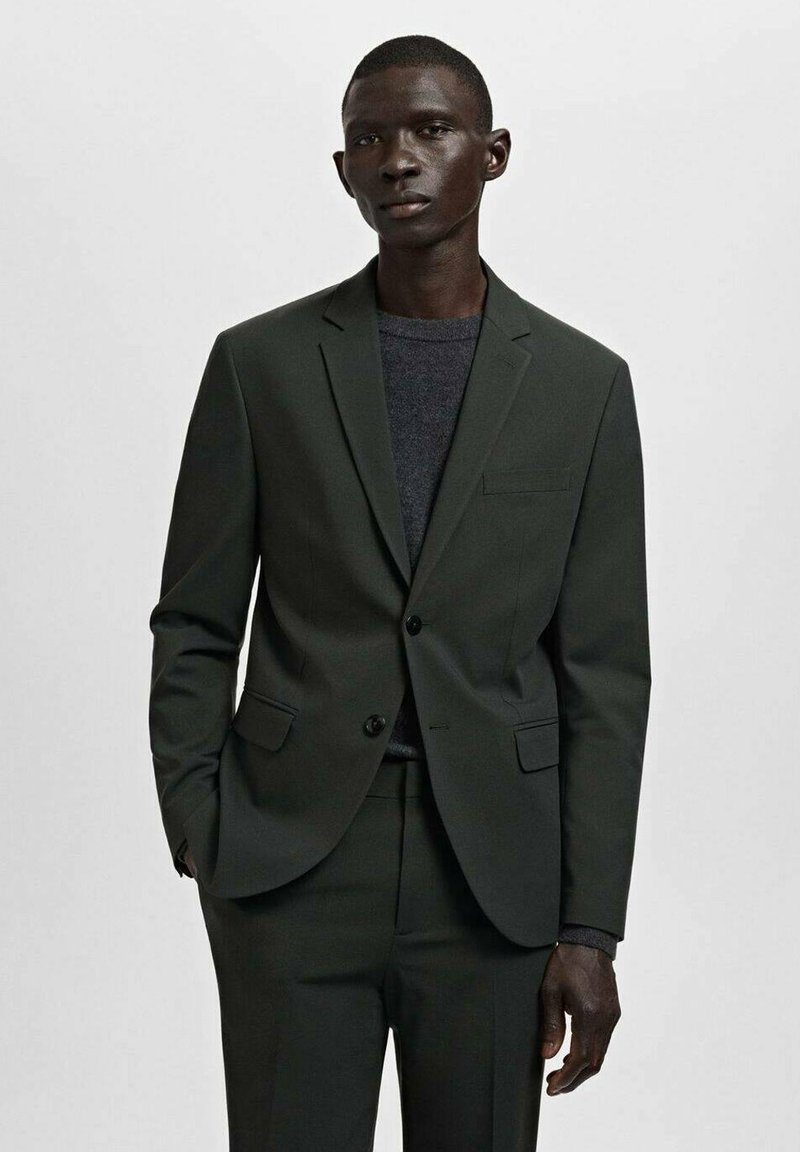 Dunkelgrüne Anzugjacke mit klassischem Revers, einer Brusttasche, zwei Vordertaschen und modernem Slim Fit. Grauer Pullover darunter.