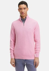 Pull demi-zip rose clair en tissu texturé avec des poignets côtelés, porté sur une chemise à motifs. Signalisation simple sur la poitrine.