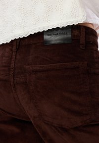Bruine corduroy broek met verticale ribbels en een zwarte leren label met de tekst "WE THE FREE" op de tailleband. Bevat details van achterzak.