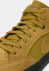 Gros plan d'une basket en daim jaune moutarde avec des lacets assortis, un bout perforé et une semelle noire.