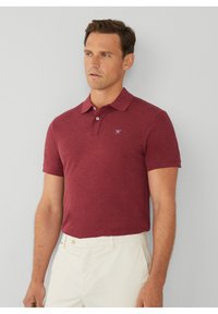 Burgundská polo košeľa s krátkymi rukávmi, s dvoma gombíkmi a malým modrým logom na hrudi. Vyrobená z mäkkého, štruktúrovaného materiálu.