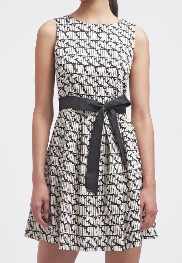 Robe sans manches avec un col rond, présentant un motif noir et blanc, taille cintrée avec une ceinture en satin noir, et jupe évasée.