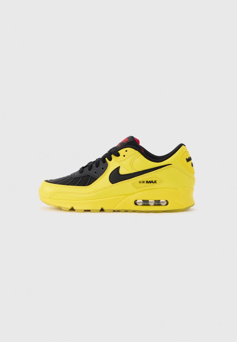 Κίτρινο και μαύρο αθλητικό παπούτσι Nike Air Max με ορατή αερόσολα και μαύρο λογότυπο Swoosh, εμφανιζόμενο από πλάγια σε απλό φόντο.