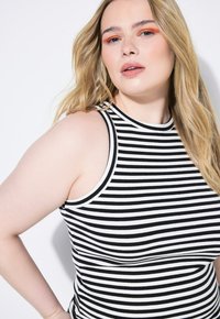 Top senza maniche a righe bianche e nere con texture a costine e scollatura alta, caratterizzato da ampi fori per le braccia e una silhouette aderente.