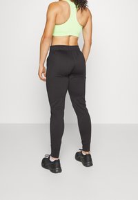 Zwarte sportieve joggers met een taperend fit, gecombineerd met een neongroene sportbeha. De outfit heeft een elastische tailleband en is gemaakt van rekbaar materiaal.