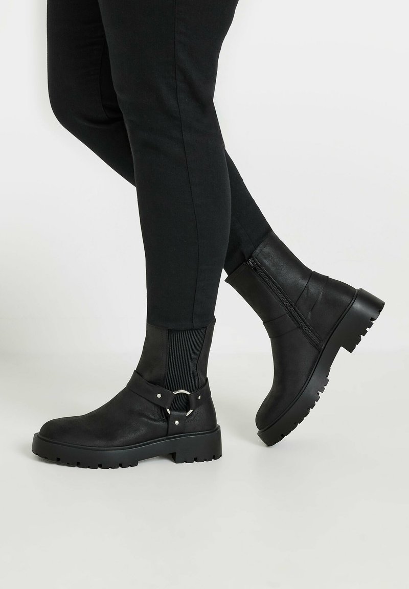 Black ankle boots with a matte finish, featuring a side zipper, chunky rubber sole, and a buckle strap detail.
