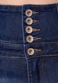 Hoge taille spijkerbroek van denim met een donkerblauwe wassing, voorzien van vijf bronzen metalen knopen en contrasterende stikdetails.