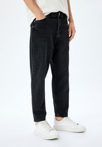 Jeans de mezclilla negra con corte recto, diseño de cinco bolsillos y una textura descolorida, combinados con zapatillas blancas.