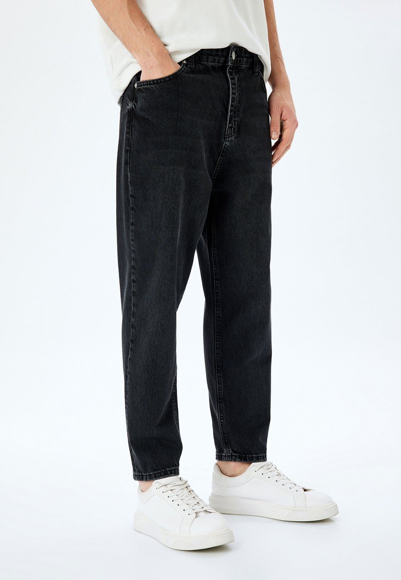 Jeans de mezclilla negra con corte recto, diseño de cinco bolsillos y una textura descolorida, combinados con zapatillas blancas.