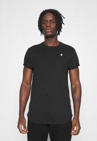 Tricou negru cu mânecă scurtă și gât rotund, având un logo mic pe piept. Material moale cu o textură netedă.