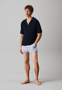 Mörkblå kortärmad polo med en texturerad stickad struktur, prydd med V-hals och kontrasterande krage; matchad med ljusgrå simshorts.