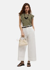 Olivgrön ribbad topp med volangärmar, vita vida byxor, svart bälte, svart pärlhalsband och beige handväska med texturerad yta.