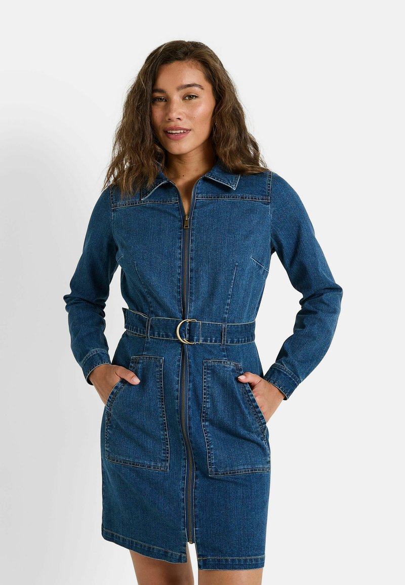 Vestido de camisa de mezclilla con cierre de cremallera completo, cintura ceñida con cinturón, dos bolsillos frontales, mangas largas y un cuello clásico en un tono azul medio.