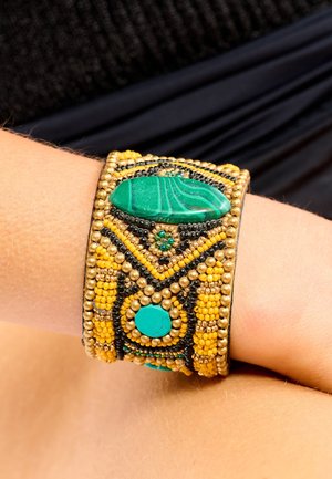 Bracelet large composé de pierres de malachite et de turquoise, avec des perles dorées et noires, des motifs complexes et une surface texturée.