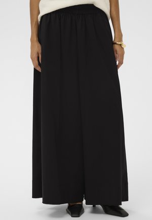 Zwarte, vloeiende maxi-rok met een elastische tailleband, voorzien van een gestructureerde stof en een gegolfde zoom. Gecombineerd met puntige zwarte schoenen.