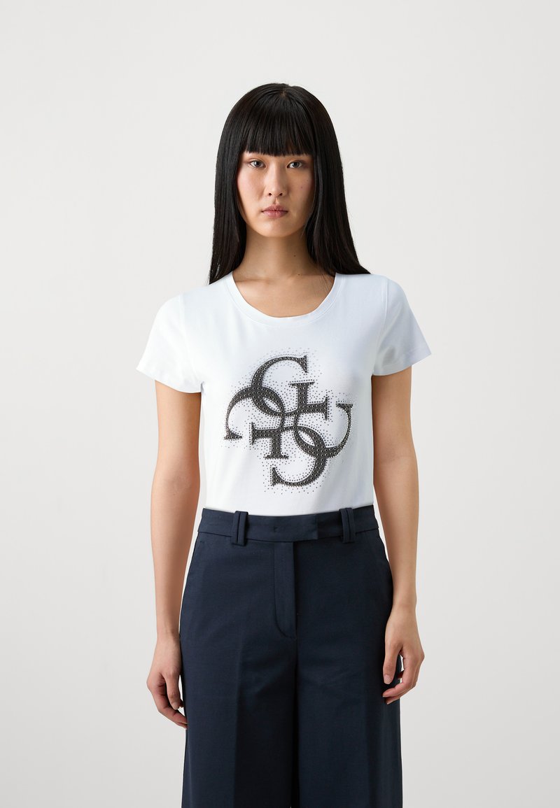 Camiseta blanca con un diseño gráfico abstracto negro en el centro, combinada con pantalones de traje azul marino. Mangas cortas, escote redondo.