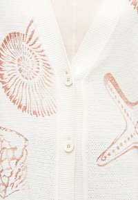 Λευκό πλεκτό ζακέτα με κούμπωμα από μπεζ κουμπιά και μοτίβα σε υφάσματα με κοραλλιογενείς, αχιβάδα, αστερία και κοράλλι σε κοραλλί χρώμα.