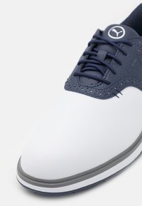 Hvit golfshoe med en jevn, matt finish. Marineblå lærdetaljer og snøringer. Perfoseringsdetaljer; grå såle med lav profil. Rundt tådesign.