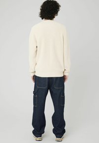 Pull en crème léger à côtes associé à un jean baggy bleu foncé avec des poches cargo. Coupe décontractée, texture en tricot et accents de couture visibles.
