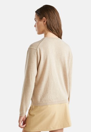 Beige gestrickter Pullover mit Rundhalsausschnitt, langen Ärmeln und gerippten Säumen. Weiche Textur mit einem leicht lockeren Schnitt, getragen über einem hellen Rock.