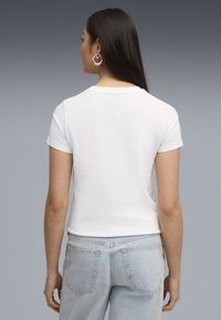 Kortærmet hvid t-shirt med rund halsudskæring, afslappet fit, parret med lyseblå denimjeans. Glat tekstur, minimalistisk design.