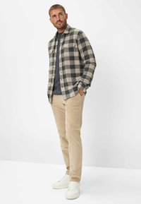 Ternet flannel skjorte i sort og beige, to brystlommer, parret med beige corduroy bukser og hvide sneakers. Struktureret stof og knapdetaljer.