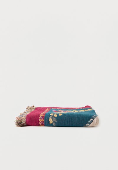 Couverture tissée pliée avec des sections bleu sarcelle et magenta, broderie florale, et bords frangés multicolores sur fond blanc.