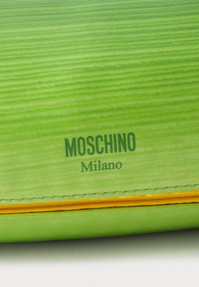 Cuir texturé vert avec logo Moschino Milano noir et bordure jaune sur un accessoire de mode.