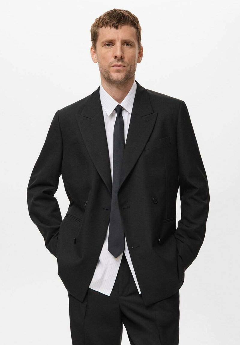 Schwarzes zweireihiges Blazer mit Revers, getragen über einem weiß-blauen gestreiften Hemd, kombiniert mit einer einfarbigen schwarzen Krawatte.