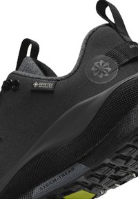 Gros plan d'une chaussure de sport noire avec une étiquette Gore-Tex Invisible Fit, une semelle texturée portant la mention "Storm Tread," et une languette au talon.