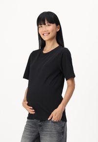 T-shirt nera a maniche corte realizzata in tessuto morbido, progettata con una vestibilità comoda per l'abbigliamento premaman, abbinata a jeans grigi.
