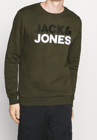 Felpa verde scuro con colletto a girocollo, caratterizzata da un grande logo testuale in bianco e nero "JACK & JONES" sulla parte anteriore. Tessuto morbido.