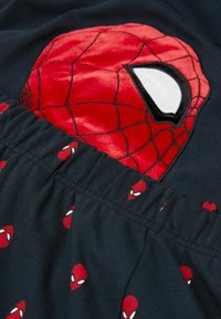 Shorts de algodón rojos y negros que presentan una gran máscara de Spiderman de felpa en el frente y pequeños logotipos de Spiderman impresos en todo su alrededor.