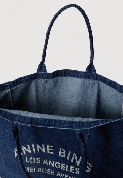 Τσάντα tote από σκουρό μπλε denim με διπλές λαβές και λευκό κείμενο που γράφει "ANINE BING LOS ANGELES MELROSE AVENUE" στην πρόσοψη.
