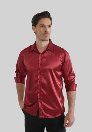 Chemise rouge en satin à manches longues avec col rabattu, fermeture par boutons sur le devant et poignets retroussés, présentant une texture lisse et brillante.