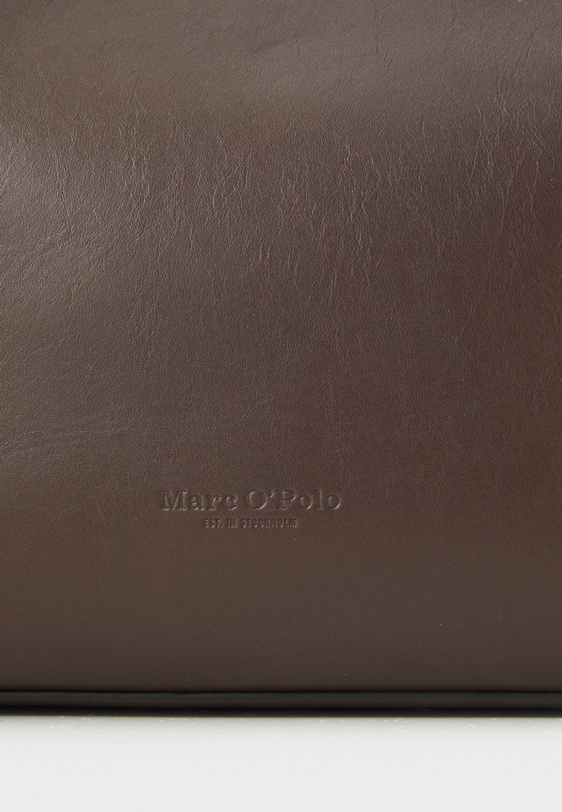 Braune Lederhandtasche mit glatter Textur, die eine geprägte Markenbezeichnung "Marc O'Polo" und das Gründungsdatum zeigt. Einfaches, minimalistisches Design.