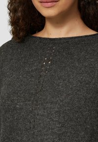 Kohlegrauer Pullover mit weicher Textur, Rundhalsausschnitt und einer vertikalen Reihe kleiner, runder Aussparungen im Brustbereich.