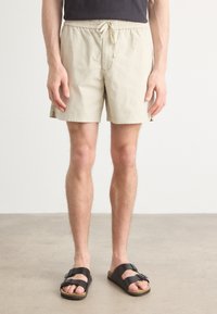 Shorts bej cu talie elastică și șnur. Fabricate dintr-un material ușor, cu buzunare laterale. Asortați cu sandale negre.