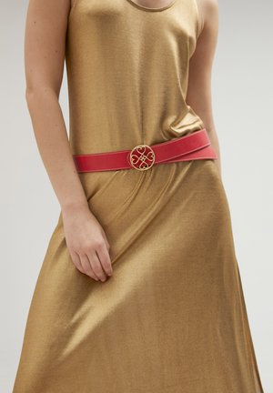 Goldfarbener metallischer Kleid mit fließender Textur, tailliert von einem breiten roten Ledergürtel mit einer runden goldenen Schnalle, die ein Herzdesign aufweist.