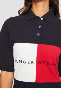 Námořnická polo tričko s barevným blokovým designem zahrnujícím bílé a červené pruhy. Knoflíky na límci a vyšívané logo "TOMMY HILFIGER NYC".
