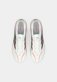 Λευκά ποδοσφαιρικά παπούτσια με μαύρες και κόκκινες λεπτομέρειες, λεία συνθετική επάνω επιφάνεια και παραδοσιακό σχέδιο με κορδόνια. Το λογότυπο είναι ορατό στη γλώσσα.