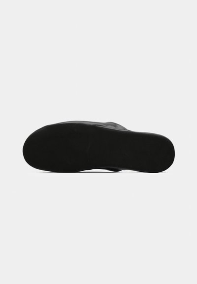 Semelle de chaussure noire avec une surface lisse et plate et des bords arrondis, vue du dessous sur un fond clair uni.