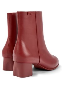 Par de botas de cuero rojas hasta el tobillo con tacones cuadrados y etiqueta del logo de Camper en la parte trasera, mostradas desde el lado trasero.
