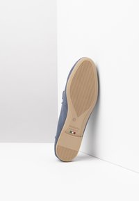 Blaues Wildlederschuh mit einer tanfarbenen Gummisohle, die ein welliges Profilmuster aufweist. Auf einem weißen Hintergrund präsentiert, wobei die Unterseite und die Seitenansicht zu sehen sind.