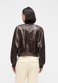 Brown faux leather bomber jacket with a ribbed hem and cuffs, featuring a smooth texture and gathered detailing along the back.