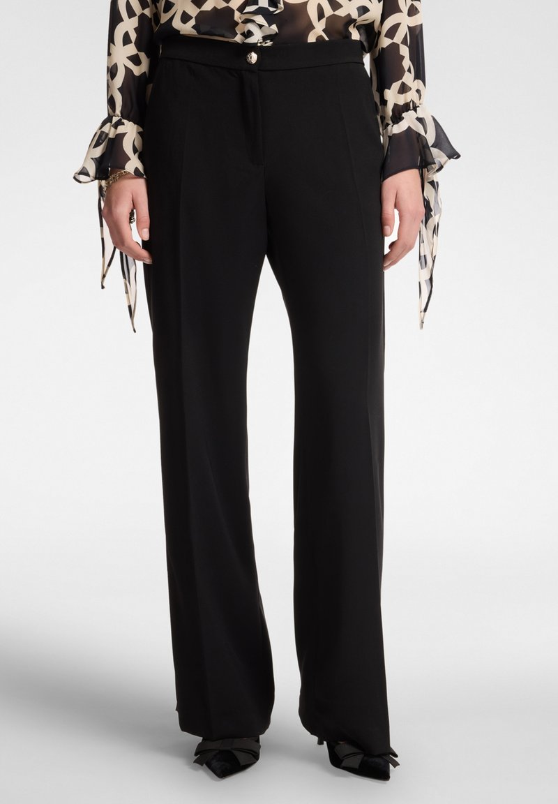 Pantaloni neri a gamba larga con una vestibilità su misura, realizzati in un tessuto morbido, con pieghe frontali e chiusura a pulsante.