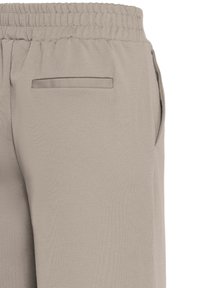 Svetlo bež jogger hlače z elastičnim pasom, ki vsebujejo zadnji žep in stranske žepne šive, narejene iz gladkega, raztegljivega materiala.